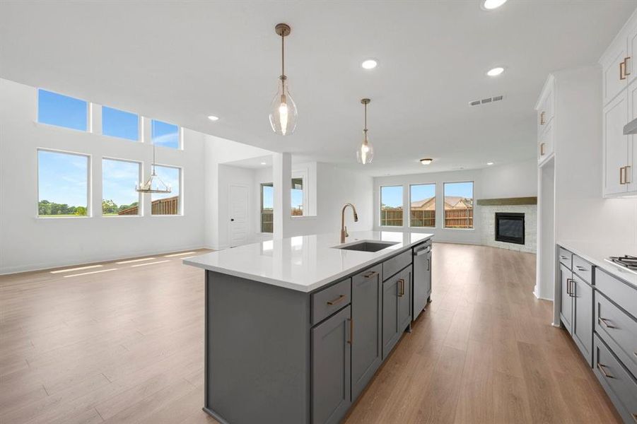 Kitchen island with a white countertop and integrated sink, pendant lighting, wood-finish flooring, a fireplace with a wood mantel, and expansive windows