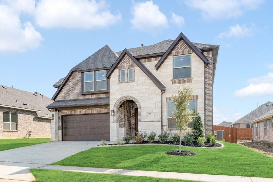 Two-story home with stone and brick exterior, arched entry, two-car garage, and manicured front lawn