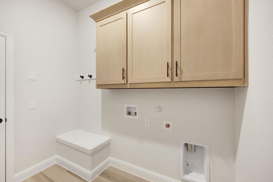 Laundry room with light wood upper cabinets, washer and dryer hookups, and built-in storage bench