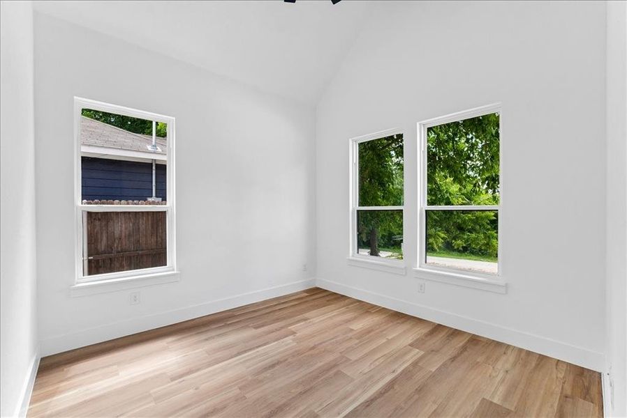 Room featuring a vaulted ceiling, light wood-finish flooring, white walls, and multiple windows Room featuring a vaulted ceiling, light wood-finish flooring, white walls, and multiple windows