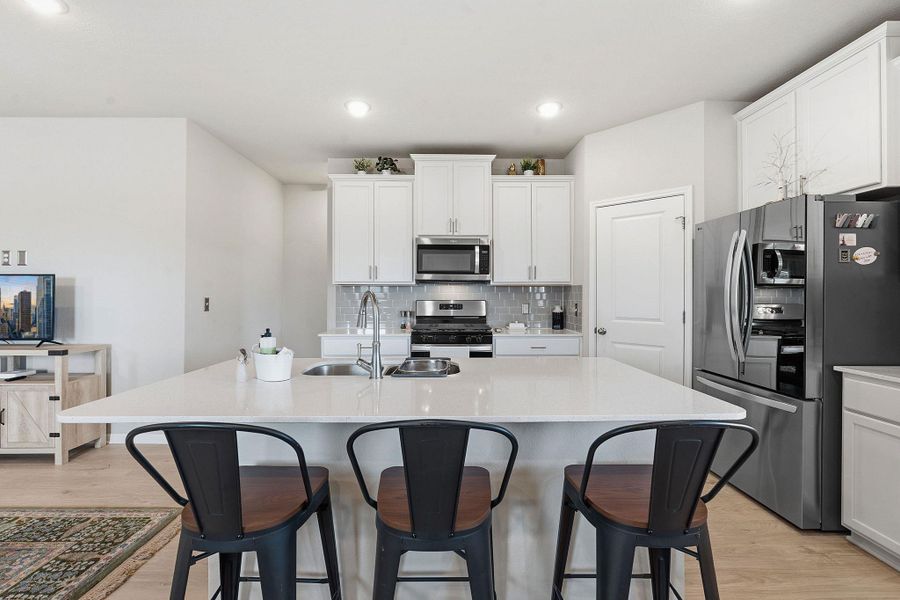 Kitchen with a kitchen breakfast bar, light wood-style floors, stainless steel appliances, white cabinetry, and recessed lighting Kitchen with a kitchen breakfast bar, light wood-style floors, stainless steel appliances, white cabinetry, and recessed lighting