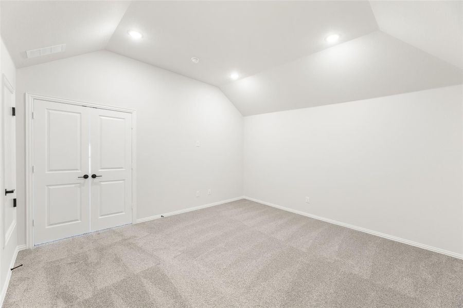 Empty bedroom with vaulted ceiling, carpet flooring, and double white closet doors