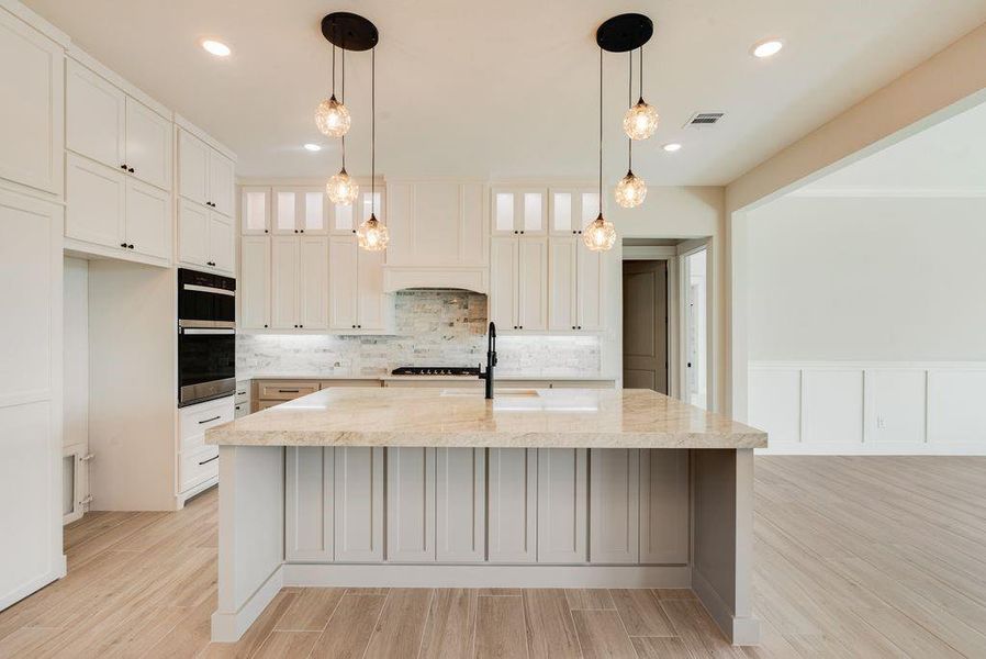 Kitchen with wood finish floors, light stone countertops, white cabinetry, a large island, and double oven