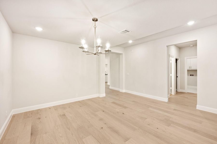 Empty dining room with light hardwood floors, white walls, and a brushed nickel chandelier