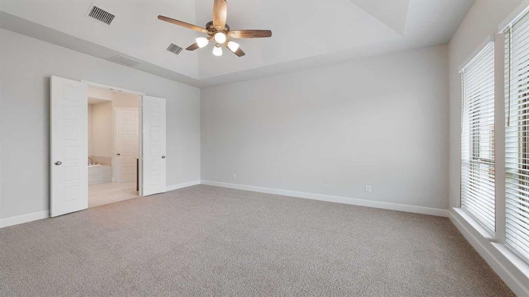 Unfurnished bedroom with light carpet, connected bathroom, a raised ceiling, and ceiling fan