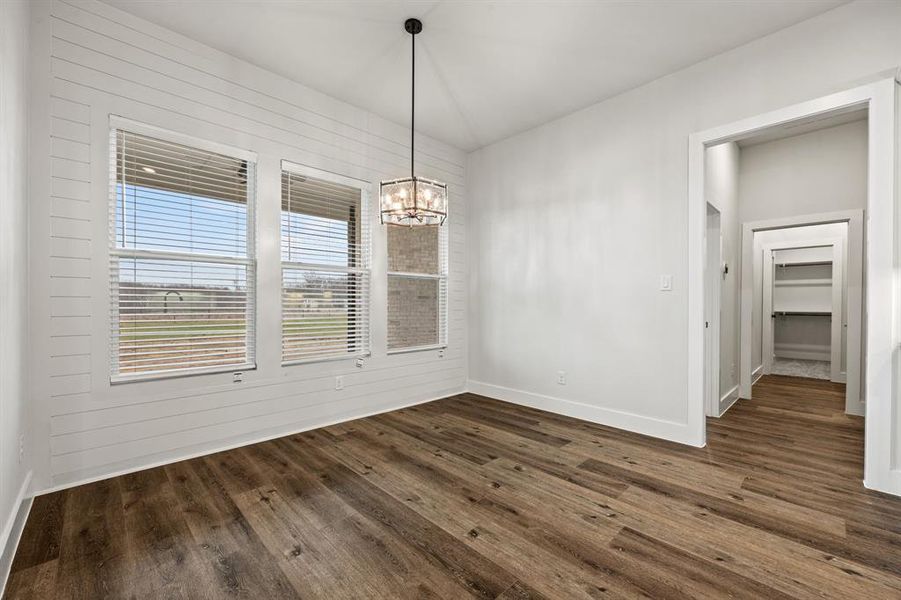 Unfurnished dining area featuring wood walls, baseboards, a chandelier, and dark wood-type flooring