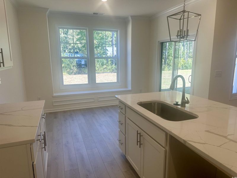 Kitchen with white cabinetry, quartz counters, light wood finished floors, hanging light fixtures, and crown molding
