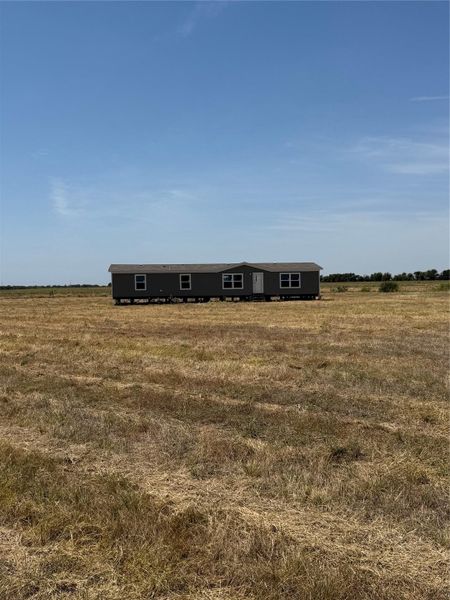 Wide open plains surround this single-level manufactured home sitting under clear blue skies.