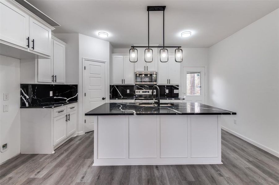 Kitchen with a center island with sink, hanging light fixtures, decorative backsplash, white cabinetry, and stainless steel appliances