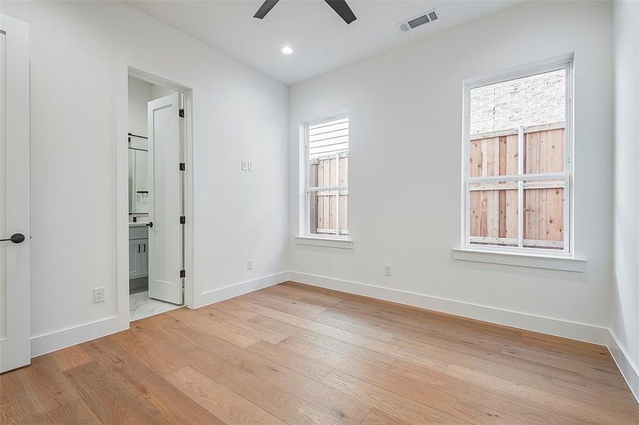 Guest room featuring windows, ensuite bathroom, ceiling fan, and light hardwood / wood-style floors