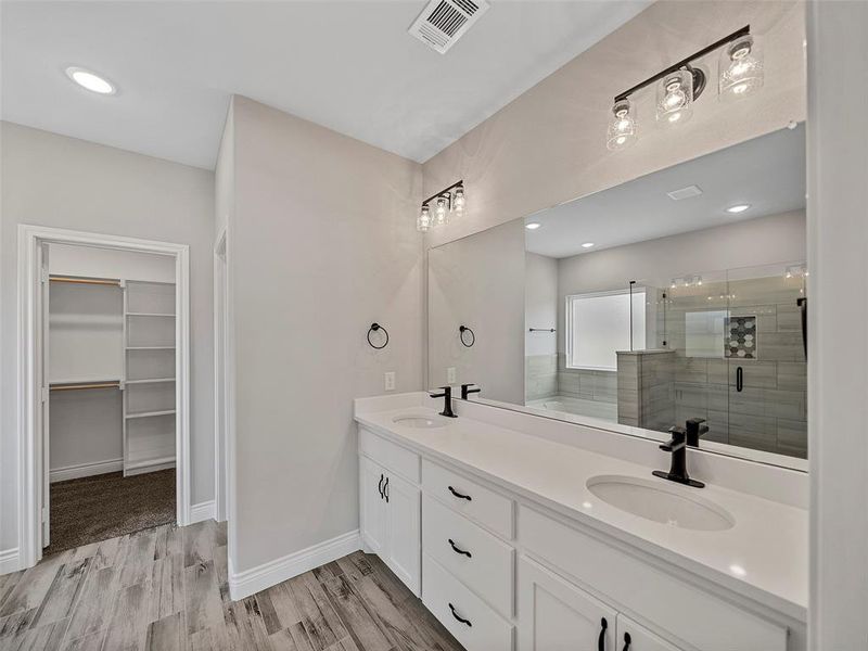 Full bath featuring recessed lighting, a shower stall, double vanity, a spacious closet, and light wood-style floors Full bath featuring recessed lighting, a shower stall, double vanity, a spacious closet, and light wood-style floors