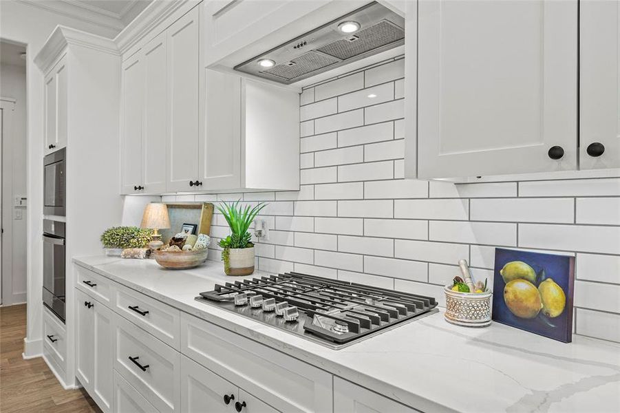 Kitchen with stainless steel gas cooktop, decorative backsplash, hardwood / wood-style flooring, and white cabinets