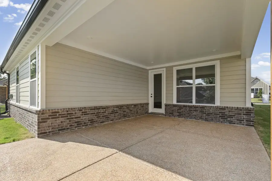 Expansive covered patio with exposed aggregate concrete flooring, featuring brick and siding exterior, and a glass-paneled door Expansive covered patio with exposed aggregate concrete flooring, featuring brick and siding exterior, and a glass-paneled door