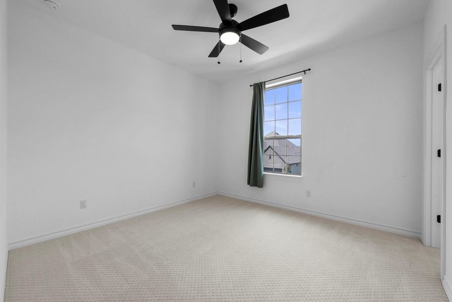 Bright bedroom with neutral carpet, ceiling fan, and large window for natural light.