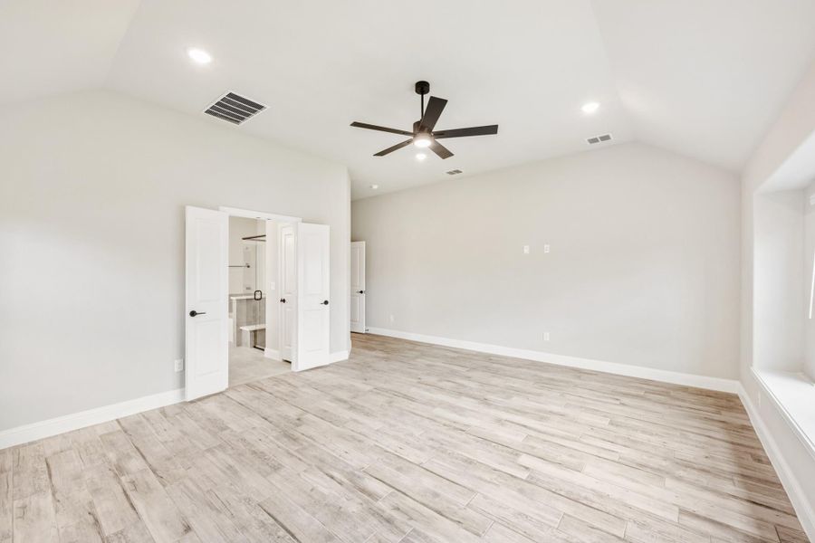 Empty bedroom with light wood floors, ceiling fan, and open doors to a walk-in closet and bathroom