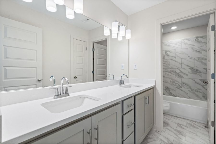 Full bathroom with double vanity, light marble finish flooring, and tub / shower combination