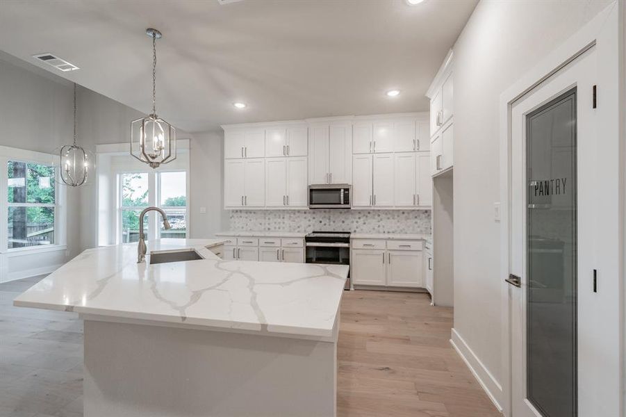 Kitchen featuring tasteful backsplash, light wood-type flooring, decorative light fixtures, white cabinets, and light stone countertops