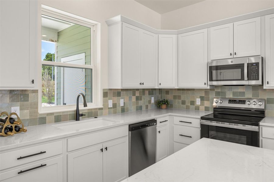 A well-appointed kitchen showcasing elegant white cabinetry, durable countertops, and a modern tile backsplash.