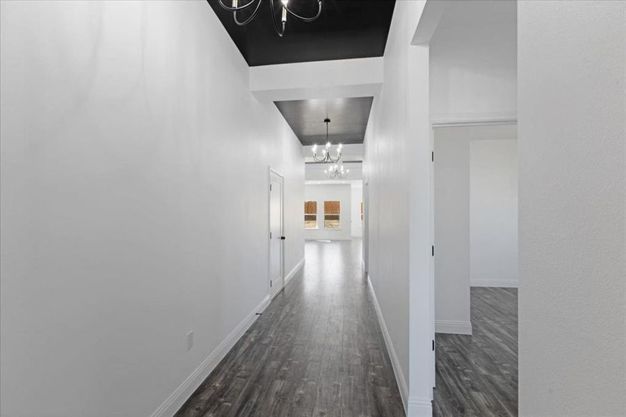 Hallway featuring baseboards, dark wood finished floors, and an inviting chandelier