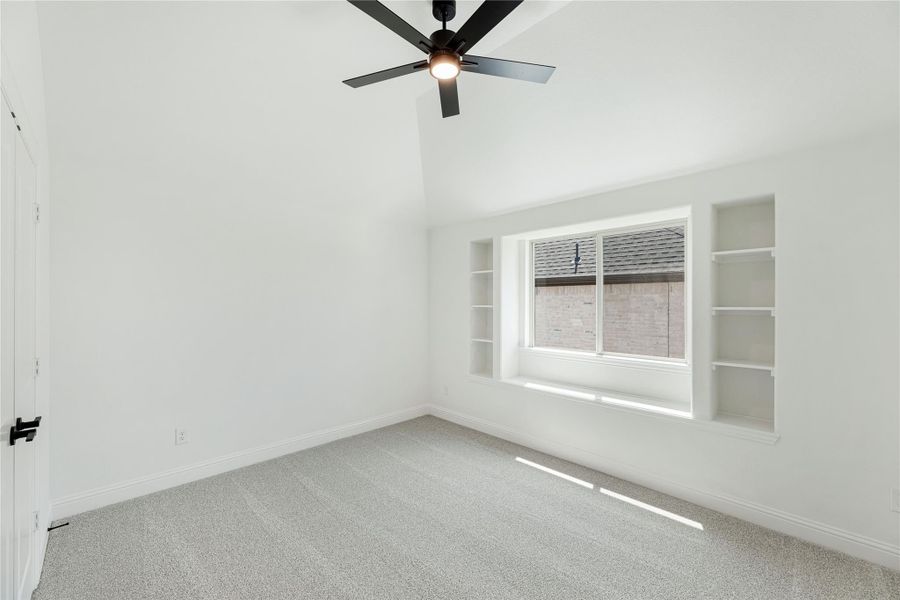 Empty bedroom with vaulted ceiling, black ceiling fan, built-in shelves, and carpet flooring Empty bedroom with vaulted ceiling, black ceiling fan, built-in shelves, and carpet flooring