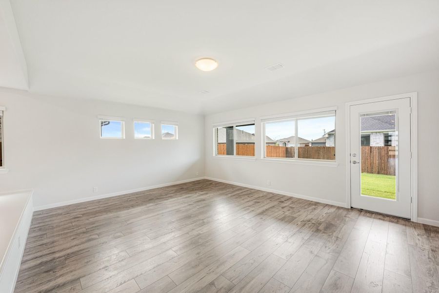 Empty living room with light wood floors, white walls, large windows, and a back door