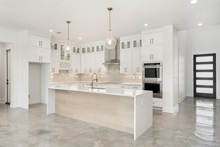 Kitchen with finished concrete floors, light stone counters, a kitchen island with sink, wall chimney range hood, and recessed lighting Kitchen with finished concrete floors, light stone counters, a kitchen island with sink, wall chimney range hood, and recessed lighting