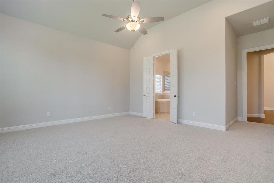 Unfurnished bedroom with light colored carpet, connected bathroom, lofted ceiling, and ceiling fan