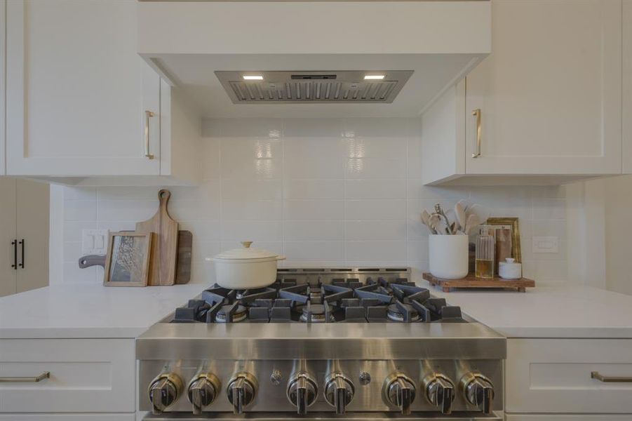 Kitchen featuring backsplash, island exhaust hood, and white cabinets