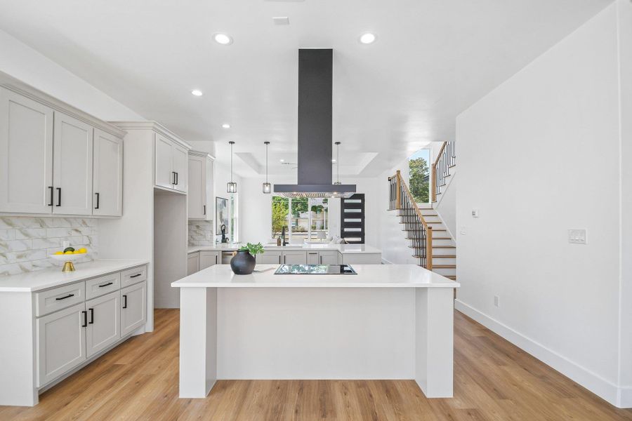 Modern kitchen with quartz-topped island and wood flooring adjacent to an open staircase. Modern kitchen with quartz-topped island and wood flooring adjacent to an open staircase.