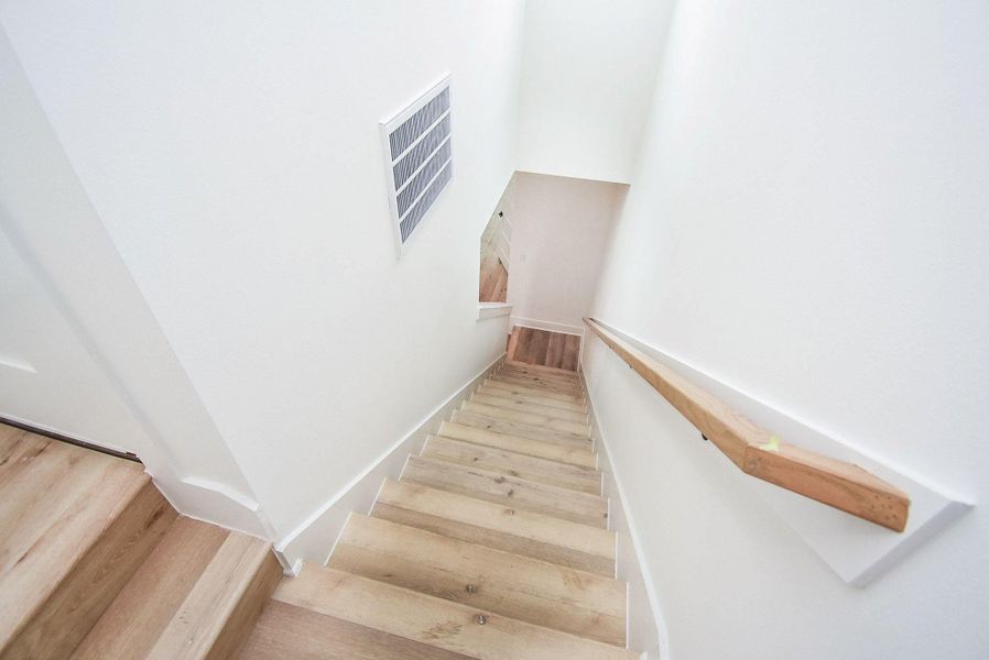 This photo shows a bright, modern staircase with wooden steps and white walls, featuring a simple handrail for support. The design is clean and minimalist, offering a welcoming pathway between floors.
