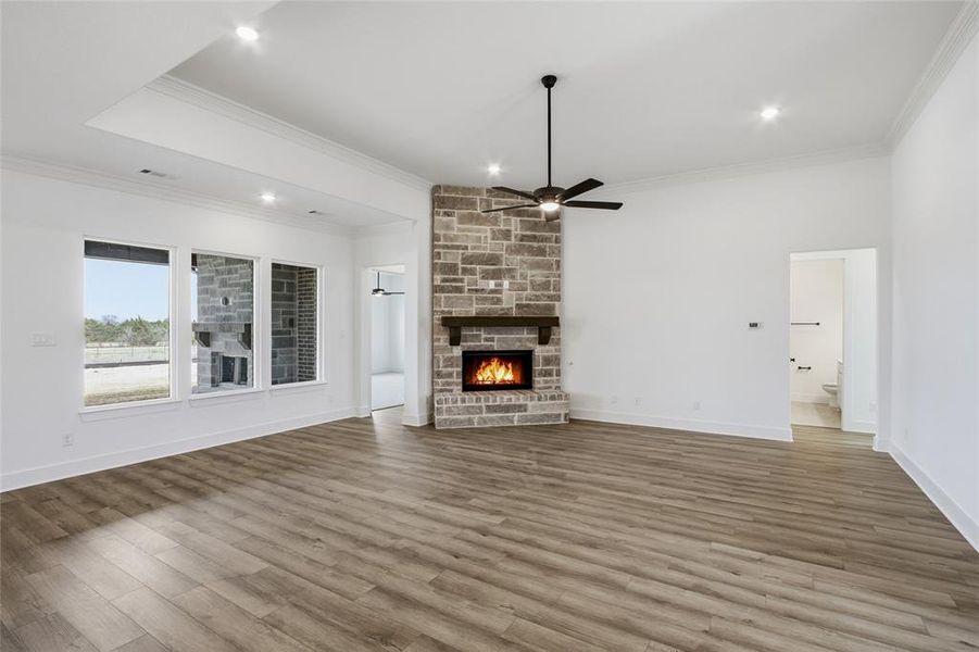 Unfurnished living room with a stone fireplace, ceiling fan, wood finished floors, ornamental molding, and recessed lighting