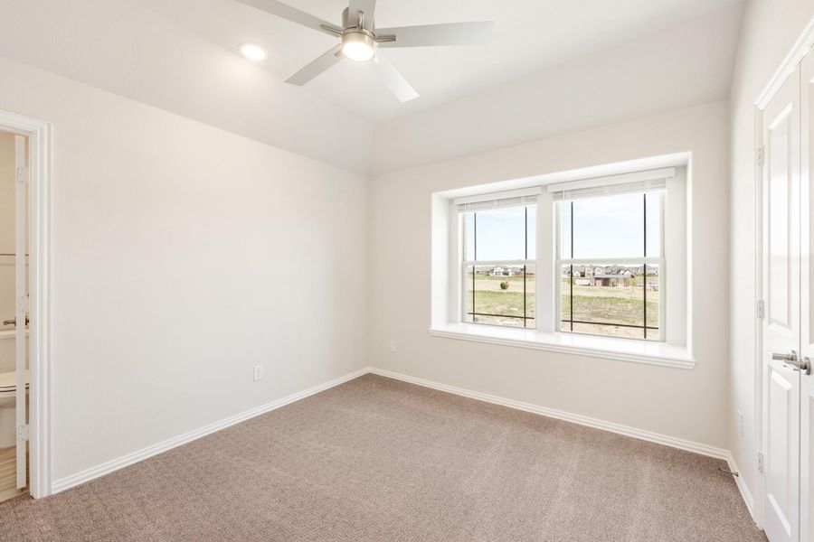 Empty bedroom with carpet, ceiling fan, double window, and adjacent bathroom door visible Empty bedroom with carpet, ceiling fan, double window, and adjacent bathroom door visible