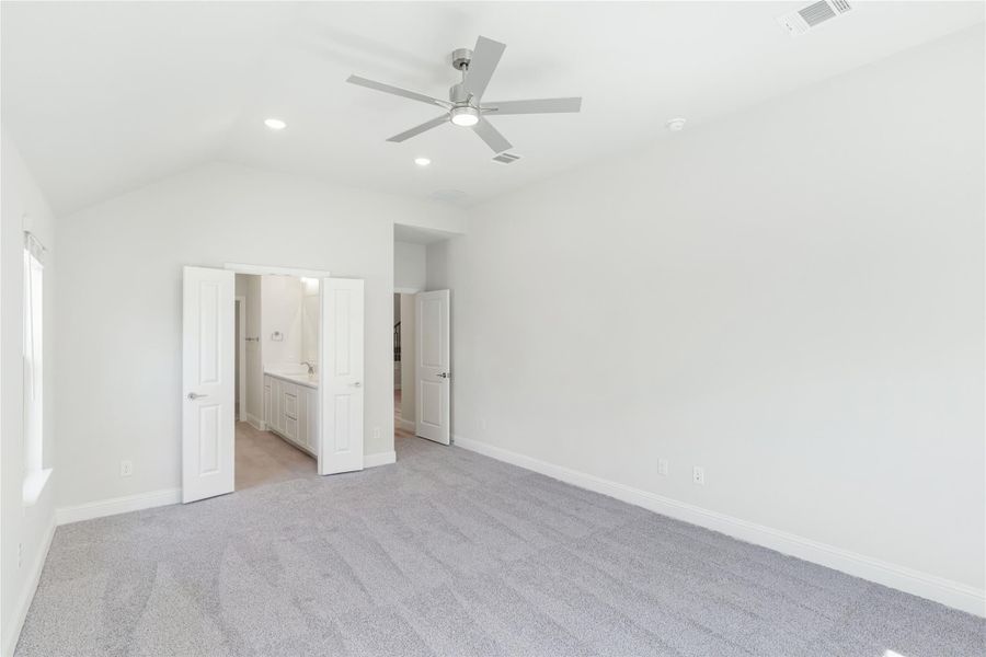 Empty bedroom with vaulted ceiling, ceiling fan, gray carpet, and open door to ensuite bathroom