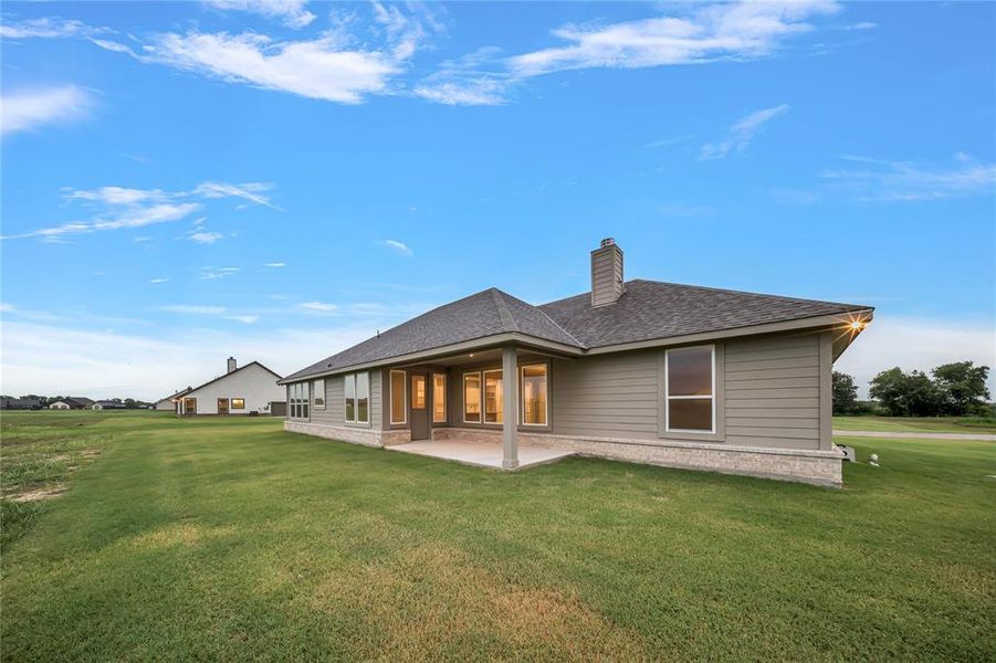 Back of property featuring a patio, a yard, a chimney, and a shingled roof Back of property featuring a patio, a yard, a chimney, and a shingled roof