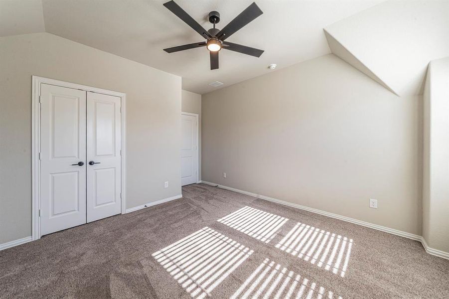 Carpeted room featuring a ceiling fan with integrated lighting, dual paneled closet doors, and sloped ceiling details