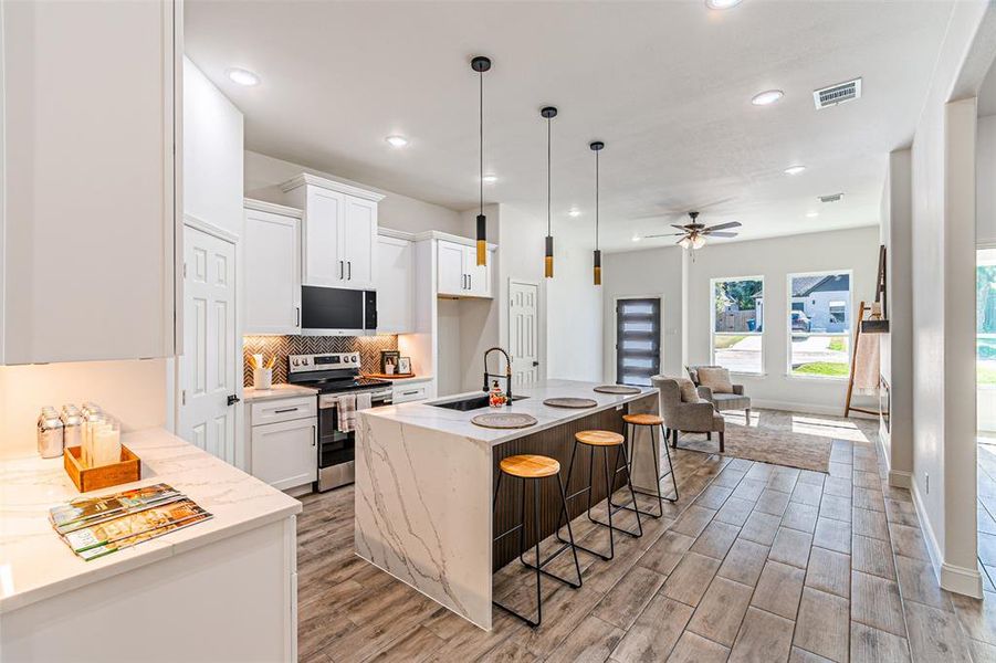 Kitchen featuring light stone countertops, appliances with stainless steel finishes, backsplash, a center island with sink, and decorative light fixtures