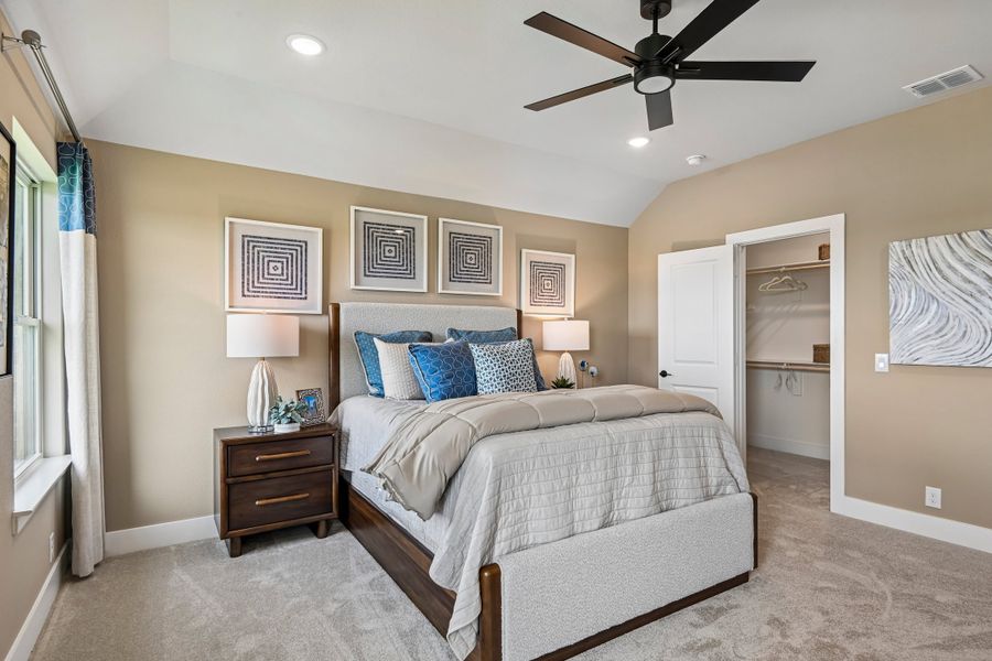 Master bedroom with vaulted ceiling, ceiling fan, carpet flooring, and walk-in closet entrance