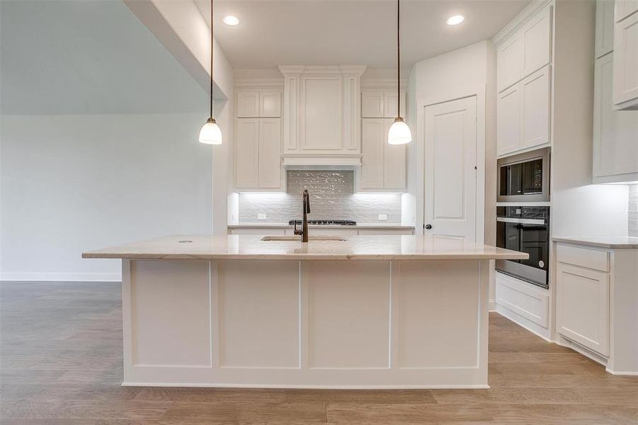 Kitchen featuring light hardwood / wood-style flooring, stainless steel oven, and a kitchen island with sink