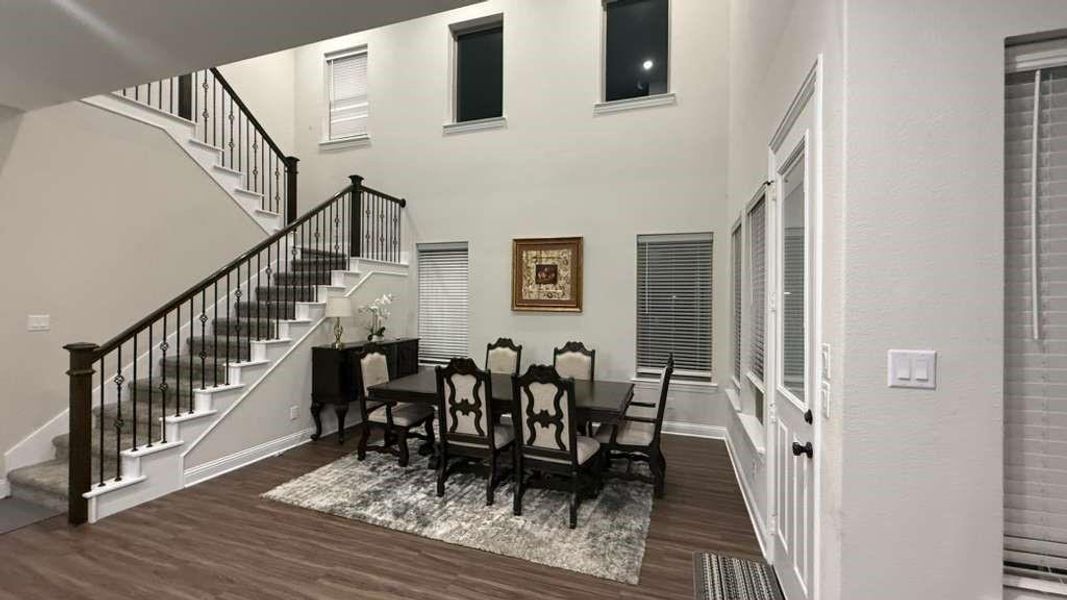 Dining area with dark wood finished floors, stairs, and a towering ceiling