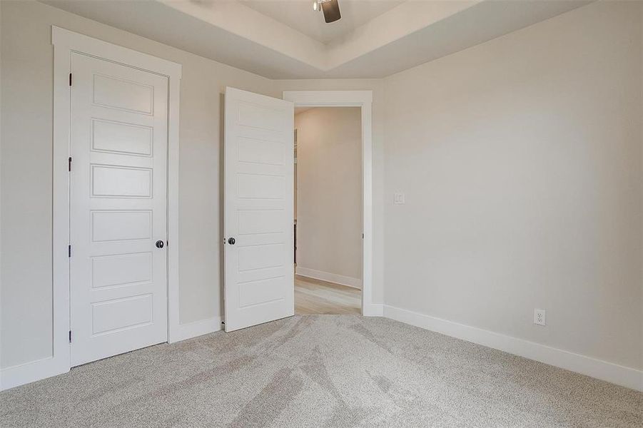 Unfurnished bedroom featuring ceiling fan, a tray ceiling, and light colored carpet