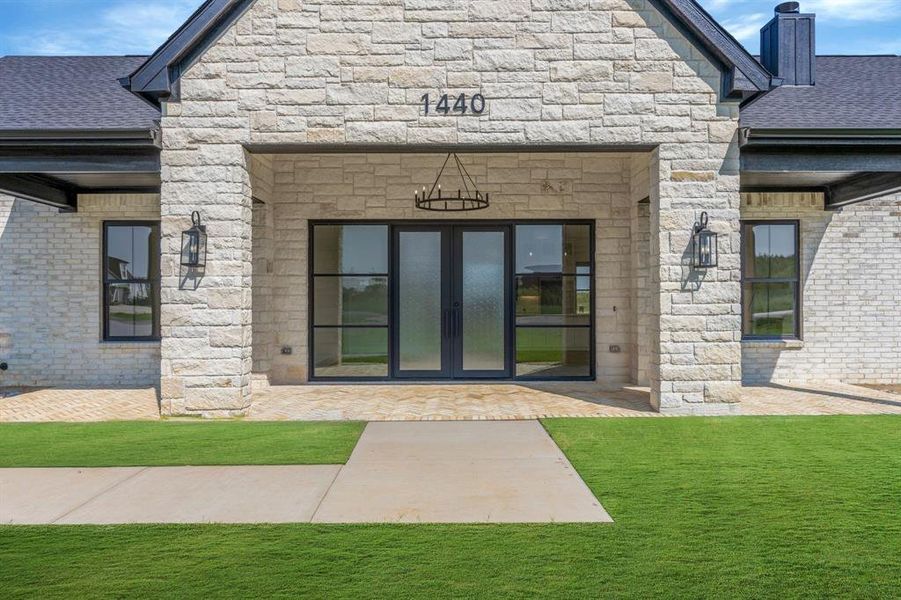 Property entrance with stone siding, custom iron and glass entry doors, a chimney, and a lawn