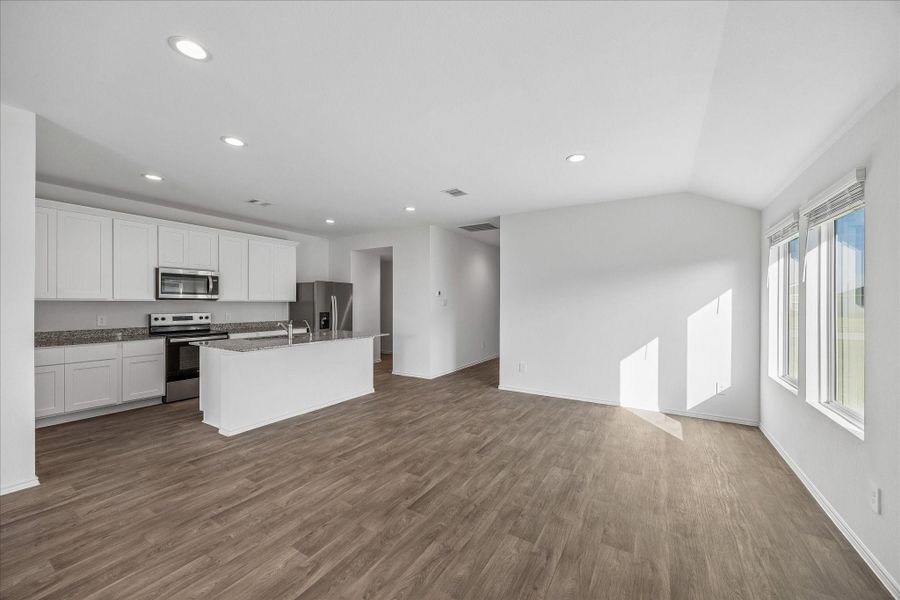 Bright, open-concept living area with modern white cabinetry in the kitchen, stainless steel appliances, and sleek hardwood flooring. Large windows allow for plenty of natural light, enhancing the spacious feel.