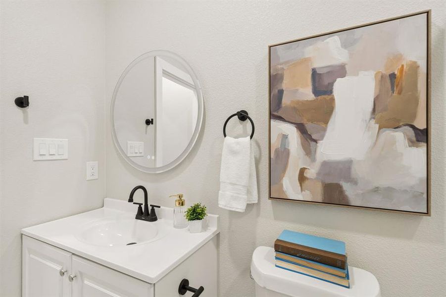 Bathroom featuring a white vanity with integrated sink, black hardware, an oval-shaped mirror, and light-toned walls Bathroom featuring a white vanity with integrated sink, black hardware, an oval-shaped mirror, and light-toned walls