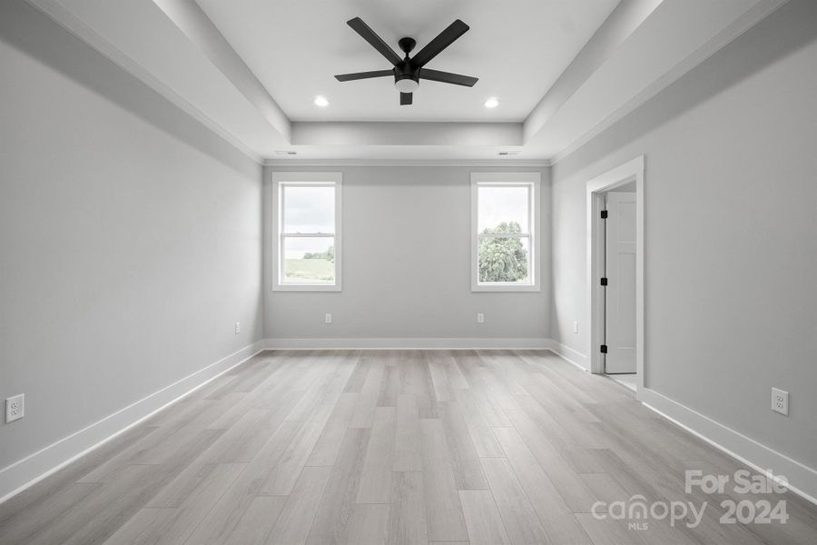 Primary bedroom with large ceiling fan and tray ceilings