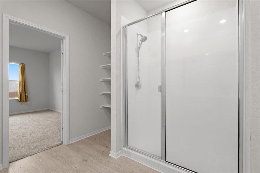 Enclosed shower with sliding glass door, modern shower head, recessed lighting, and integrated shelving