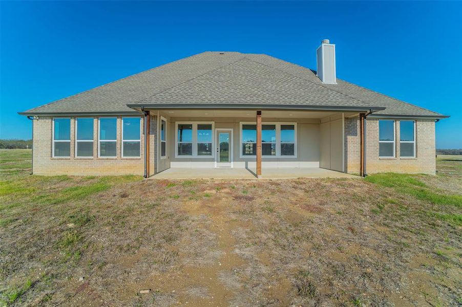 Rear view of house with a patio, a shingled roof, a chimney, a yard, and brick siding Rear view of house with a patio, a shingled roof, a chimney, a yard, and brick siding