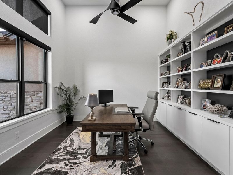 Home office with custom built-ins, dark wood finished floors and a ceiling fan