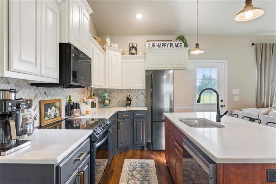 Kitchen with black appliances, decorative backsplash, dark wood finished floors, white cabinets, and a center island with sink