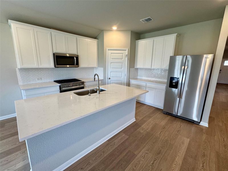 Kitchen with stainless steel appliances, white cabinetry, light stone counters, tasteful backsplash, and dark wood-type flooring