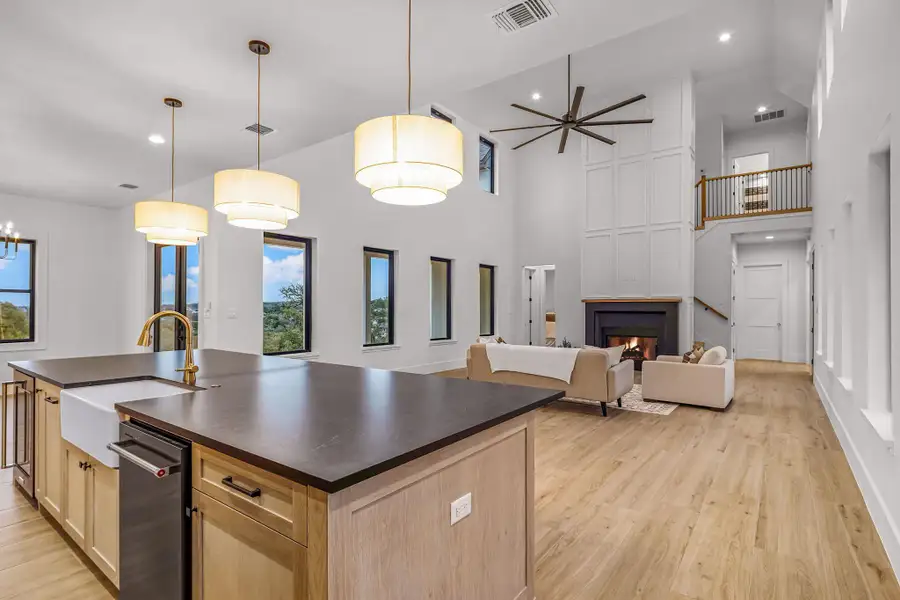 Kitchen featuring dark countertops, open floor plan, decorative light fixtures, a kitchen island with sink, and a sink